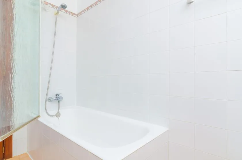 A white bathtub sits beneath tiled walls, with a handheld shower attached.