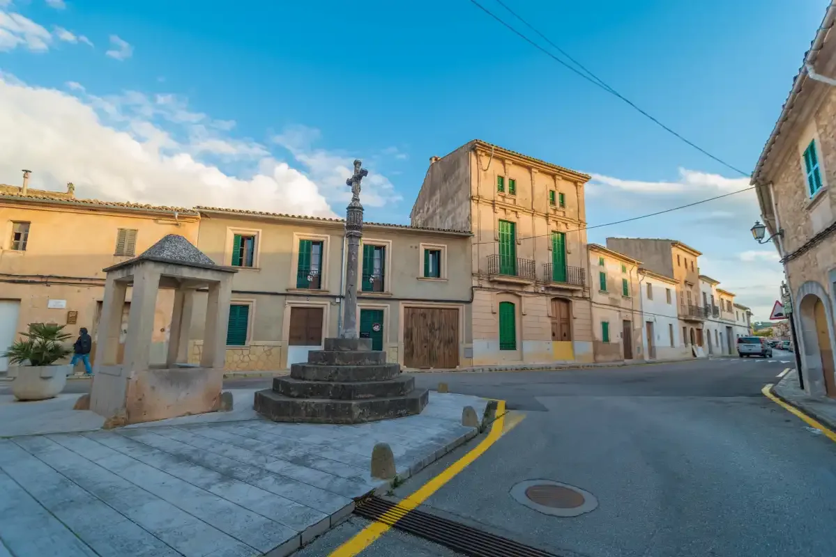 A town square with a stone monument and historic buildings along the street.
