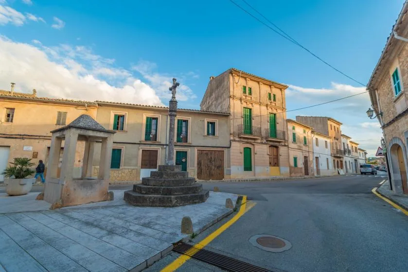 A town square with a stone monument in front of colorful buildings.