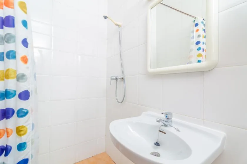 A tiled bathroom with a sink, mirror, and colorful shower curtain.