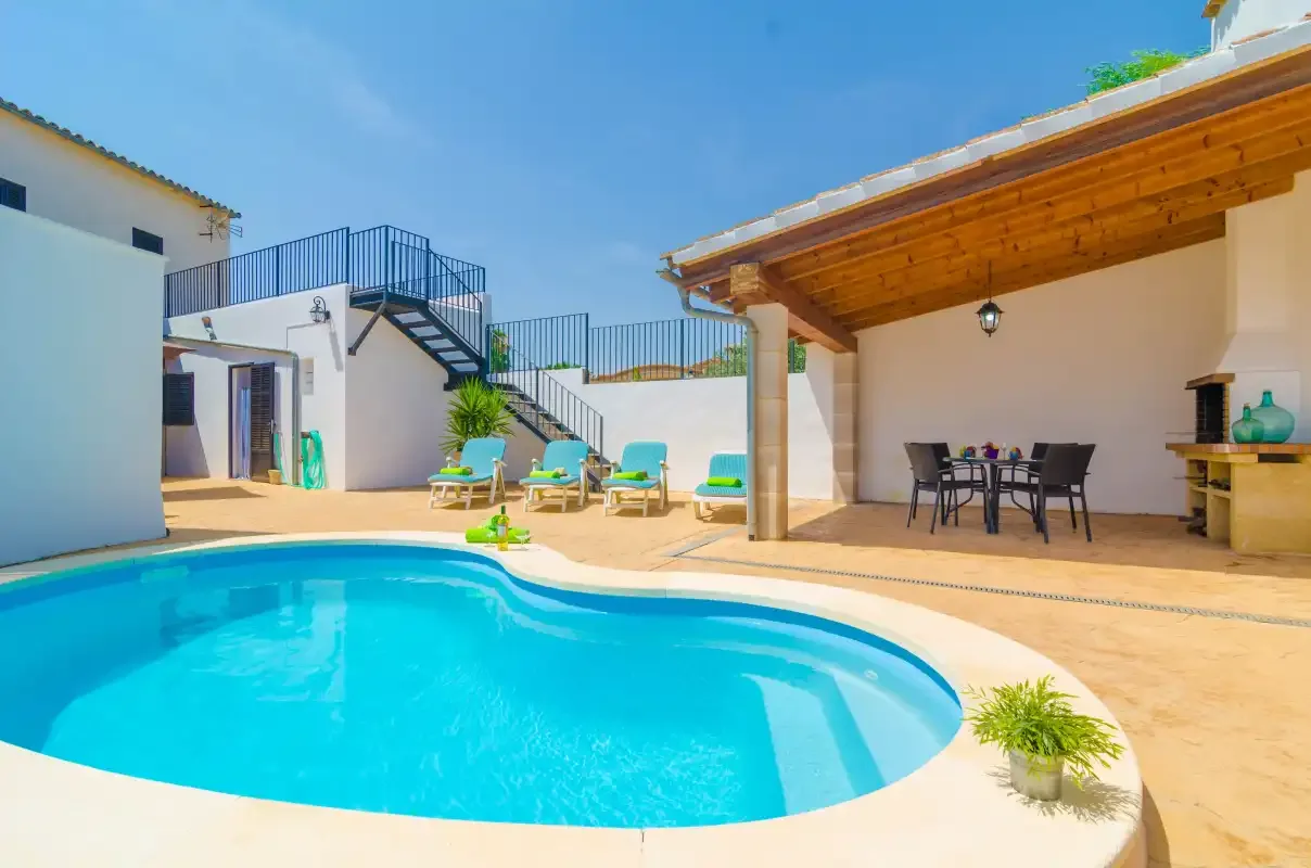 An outdoor pool sits beside a covered dining area and sun loungers.