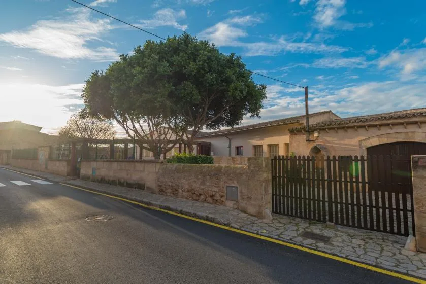 A street view of a low building behind a stone wall and gate.