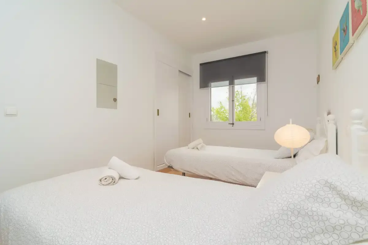 A bright bedroom with two beds and a window with a lowered shade.