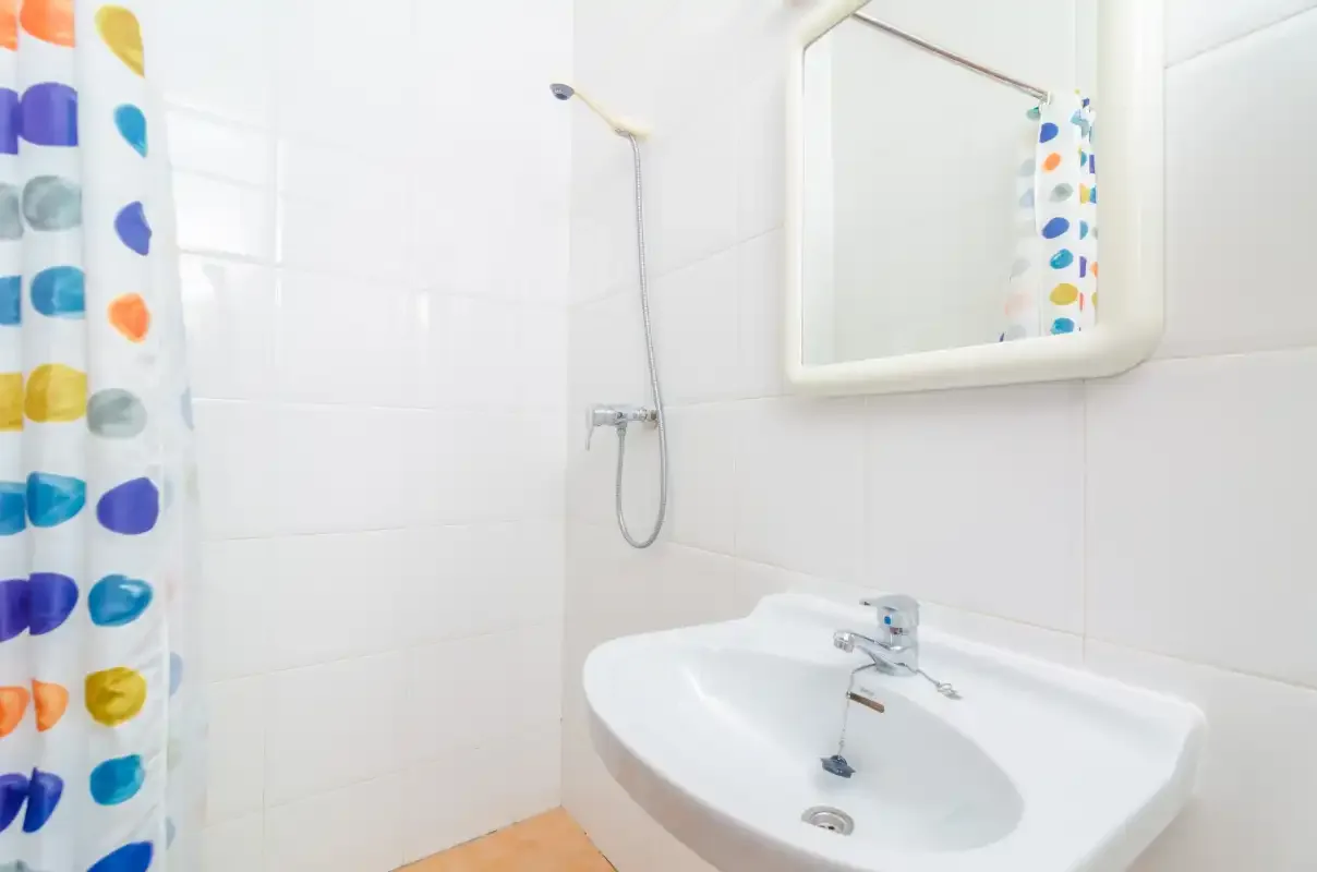 A bathroom with a white sink, mirror, and colorful shower curtain.