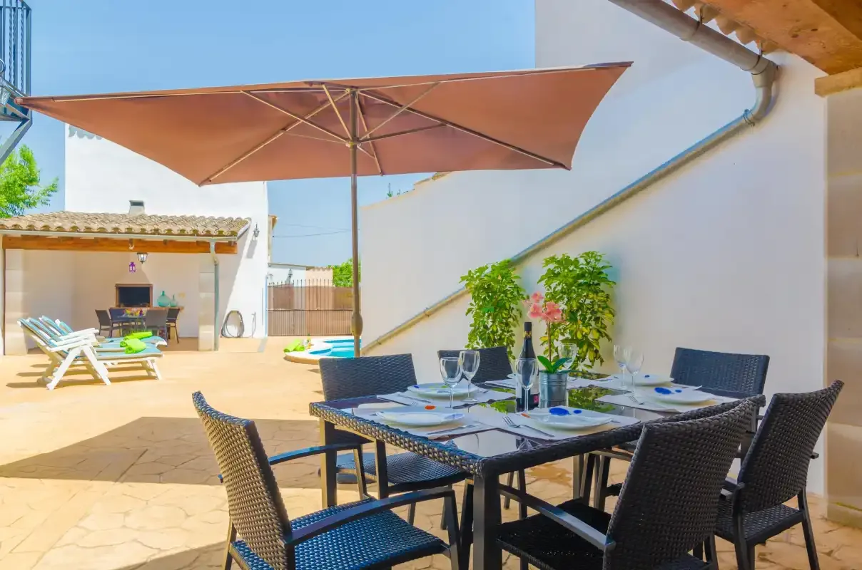 An outdoor dining area sits beneath a large patio umbrella beside a sunlit courtyard.