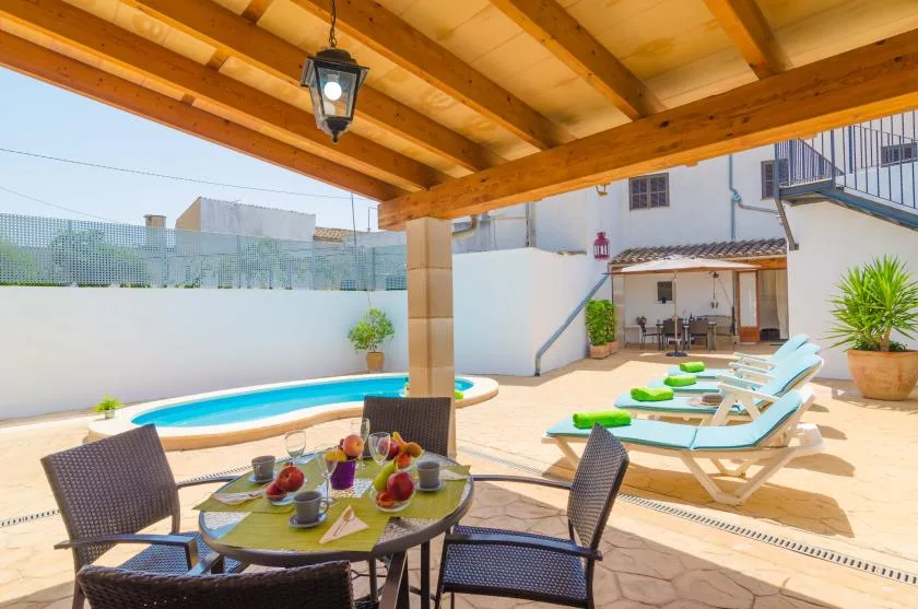 Un patio cubierto da a una pequeña piscina, con asientos y tumbonas al aire libre.