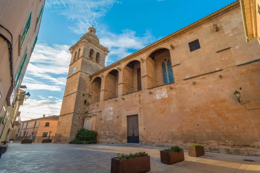 A stone church with a bell tower faces a paved plaza.