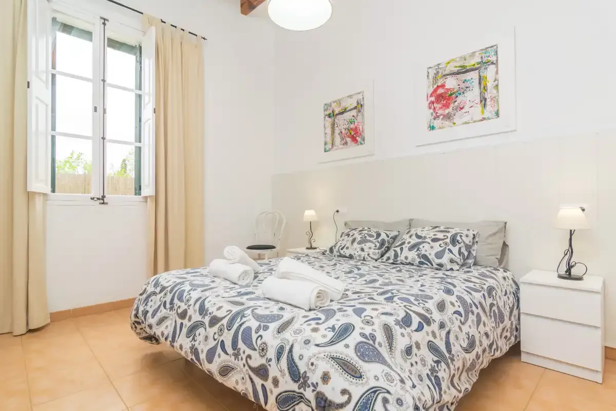 A bedroom with a patterned bedspread, bedside tables, and a curtained window.