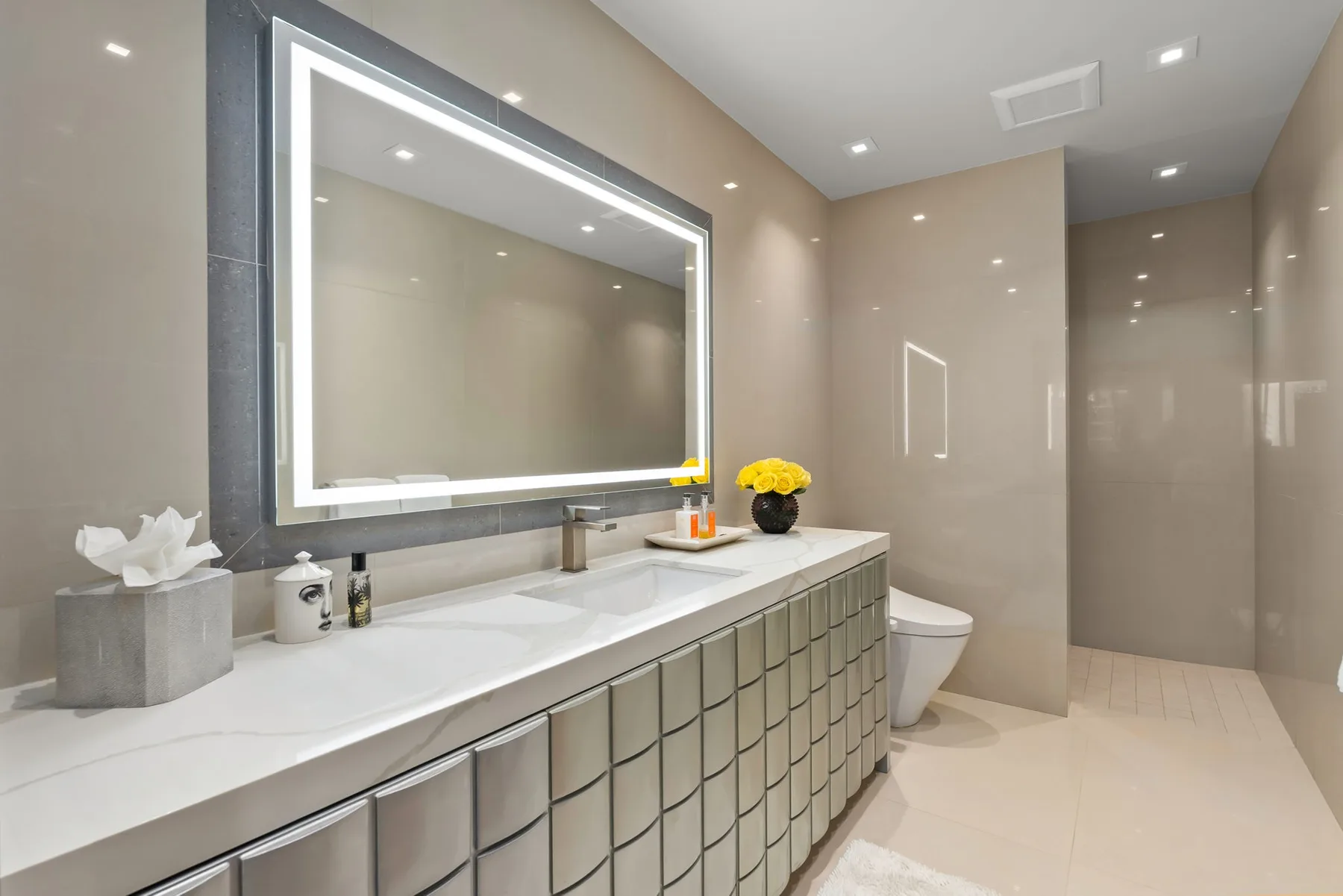 A modern bathroom with a long vanity, illuminated mirror, and shower area.