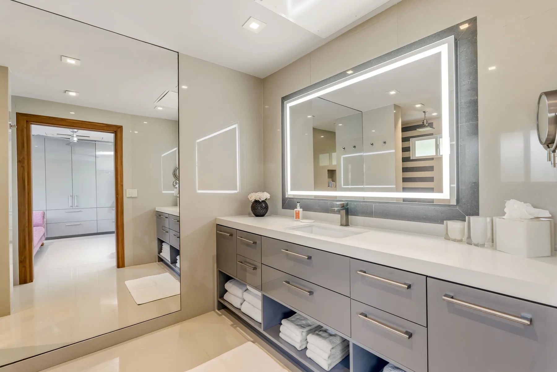 A bathroom vanity with a wide illuminated mirror and a long counter.