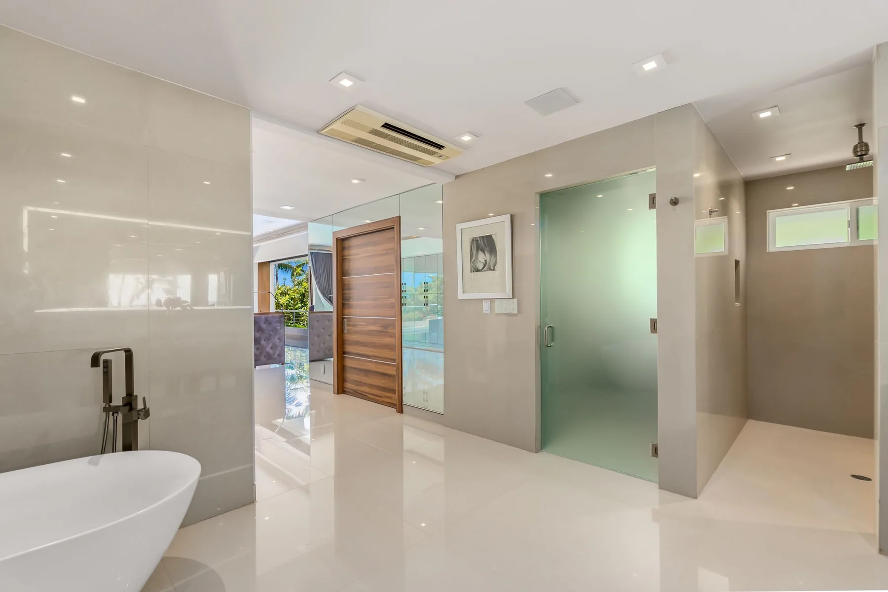 A modern bathroom with a bathtub, glass shower partition, and pale tile.