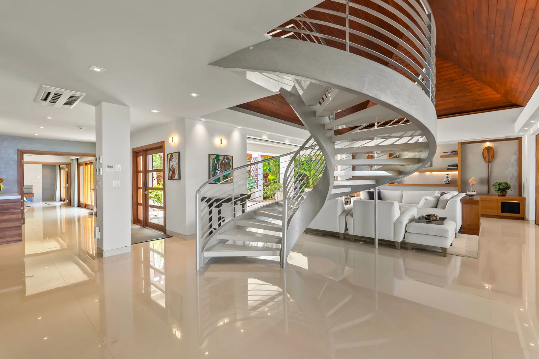 A bright open-plan living area features a curved staircase and seating.