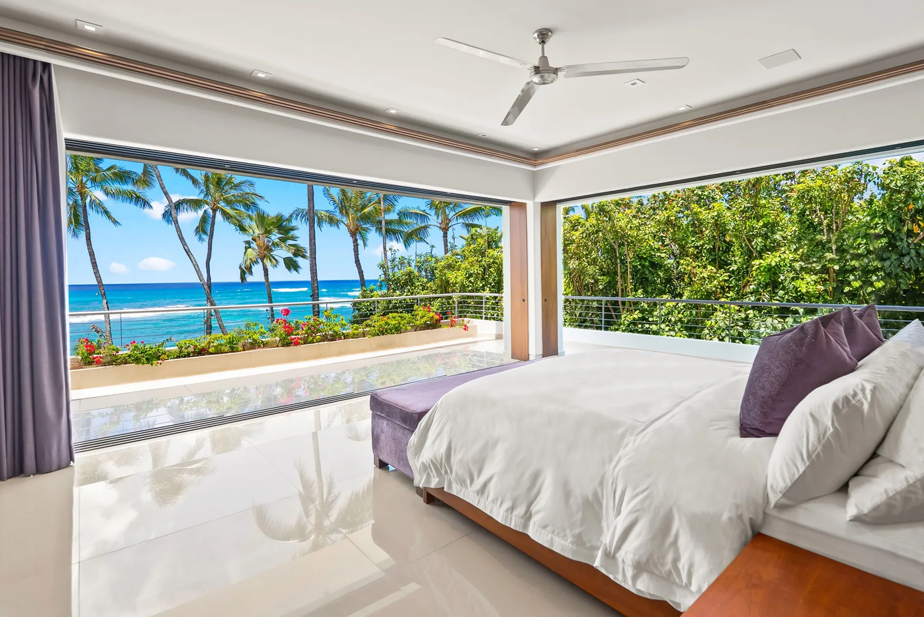A bright bedroom opens onto a balcony with tropical greenery and ocean views.