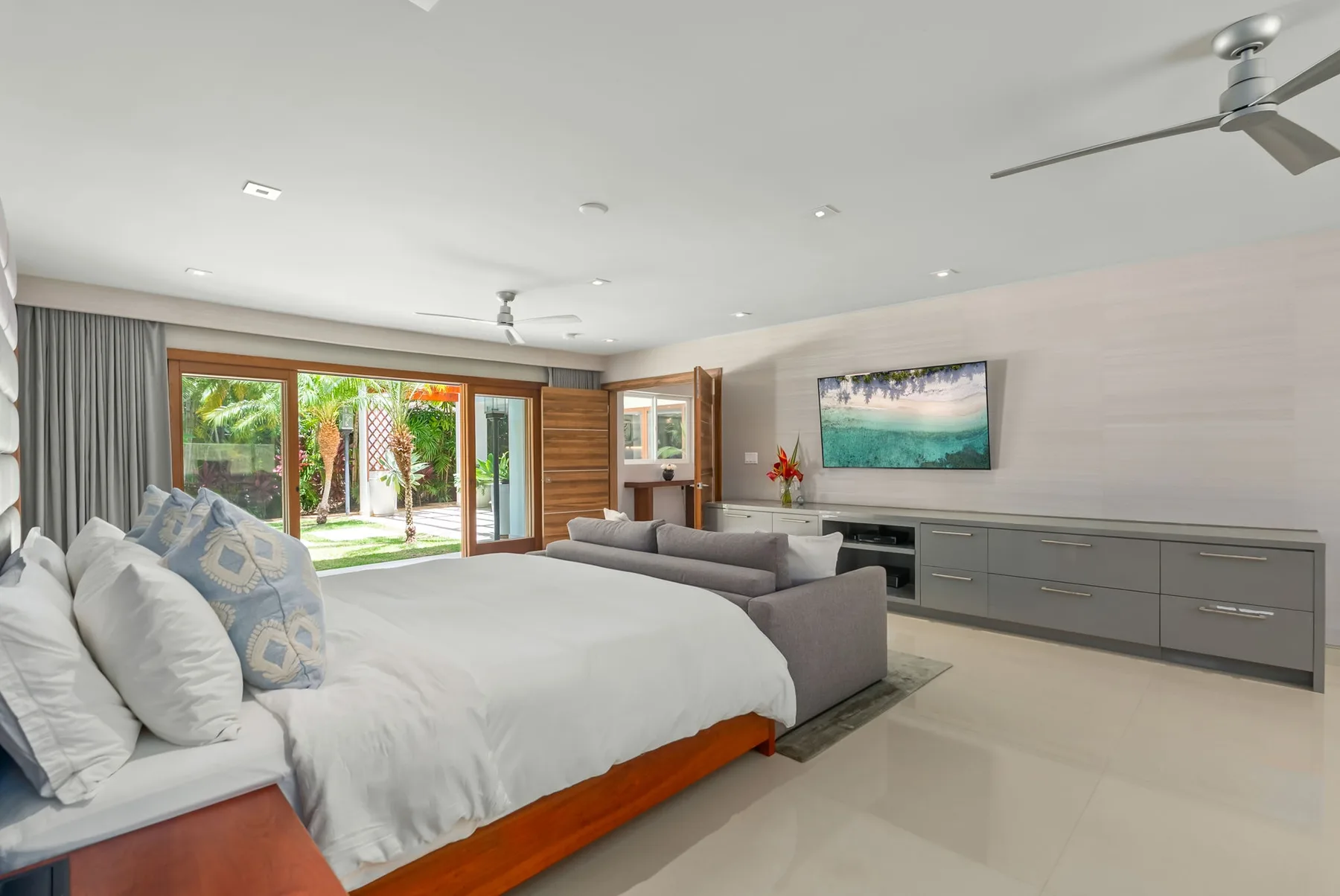 A bedroom with a large bed, seating area, and sliding glass doors opening to a garden.