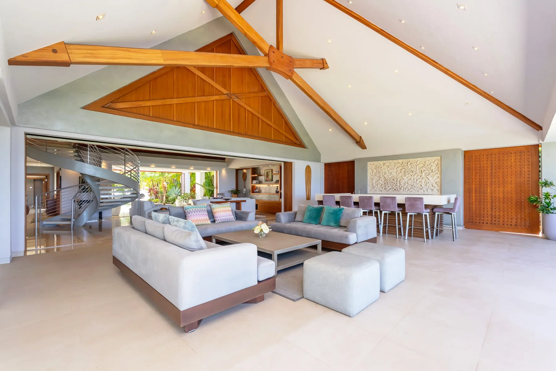 A spacious living and dining area has seating arranged beneath a high, timber-beamed ceiling.