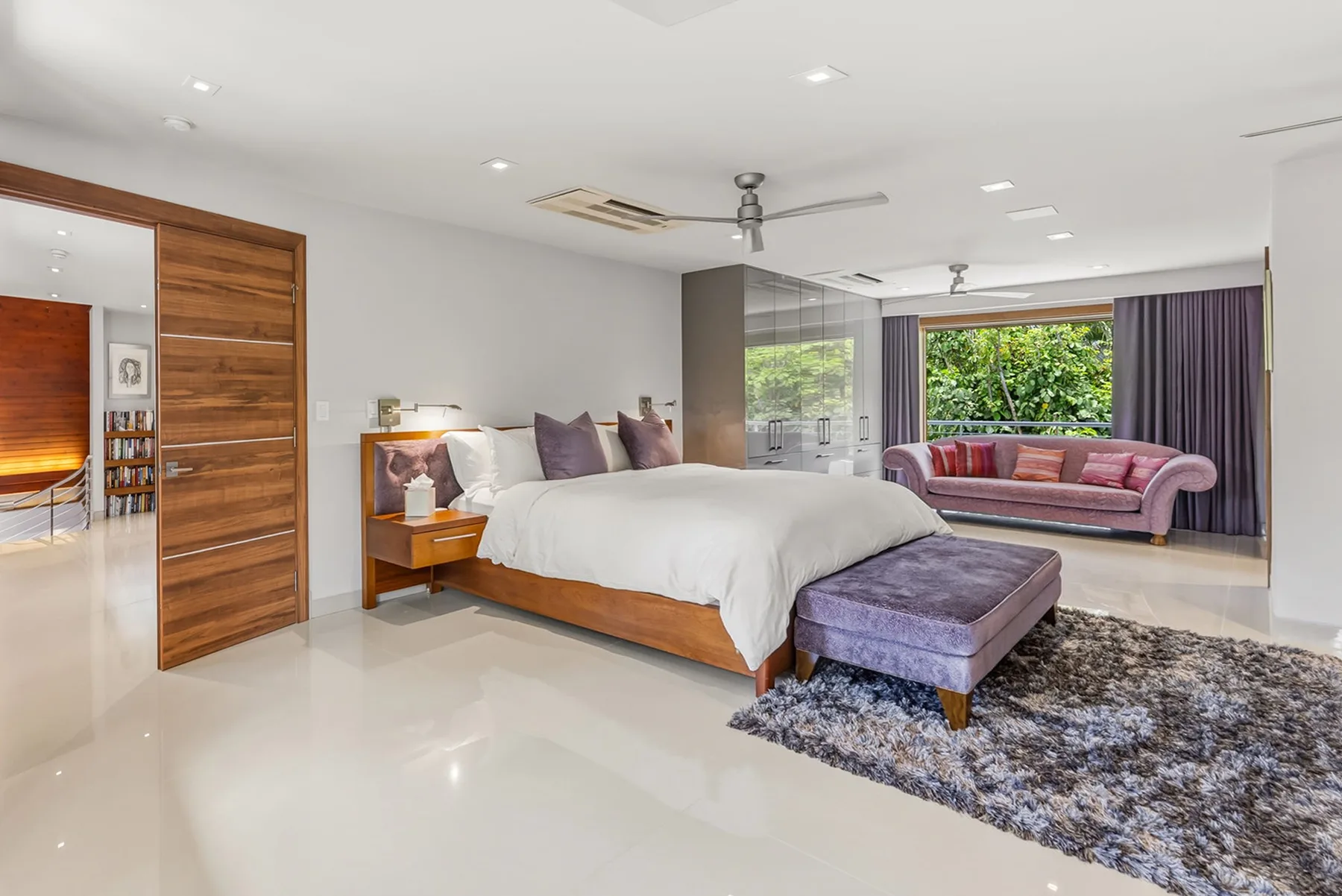 A spacious bedroom with a large bed, an upholstered bench, and a seating area by the window.
