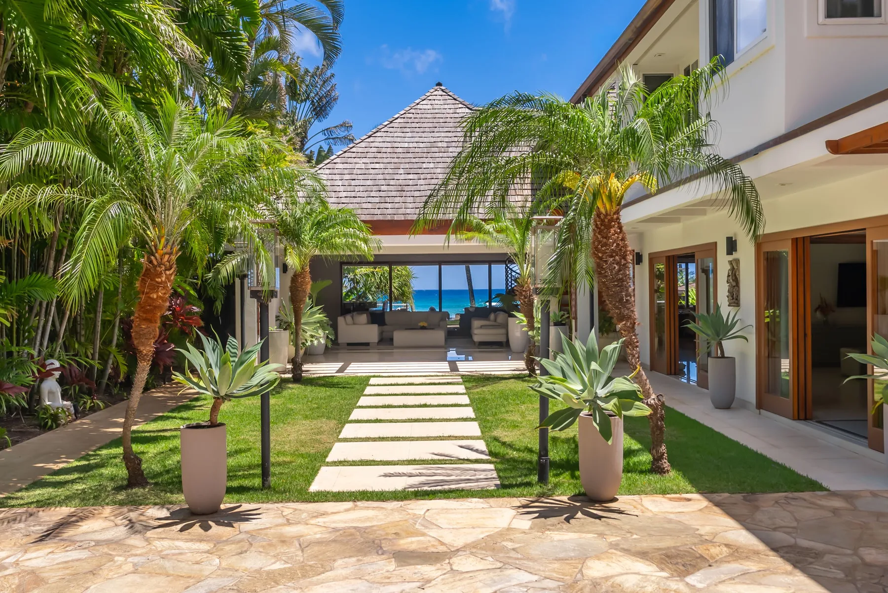 A tropical courtyard with a stone path leading toward a shaded seating area.