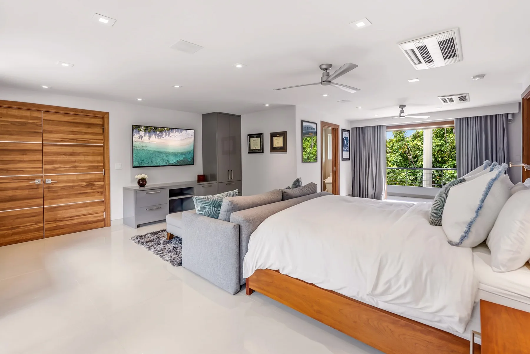 A bright bedroom with a large bed, seating area, and sliding glass doors to greenery.