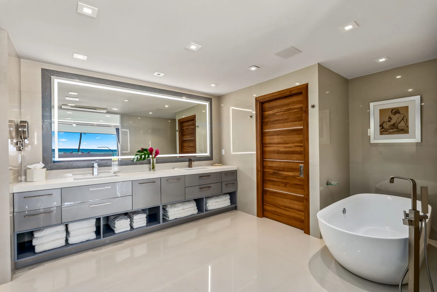 A modern bathroom with a long vanity, large mirror, and freestanding bathtub.