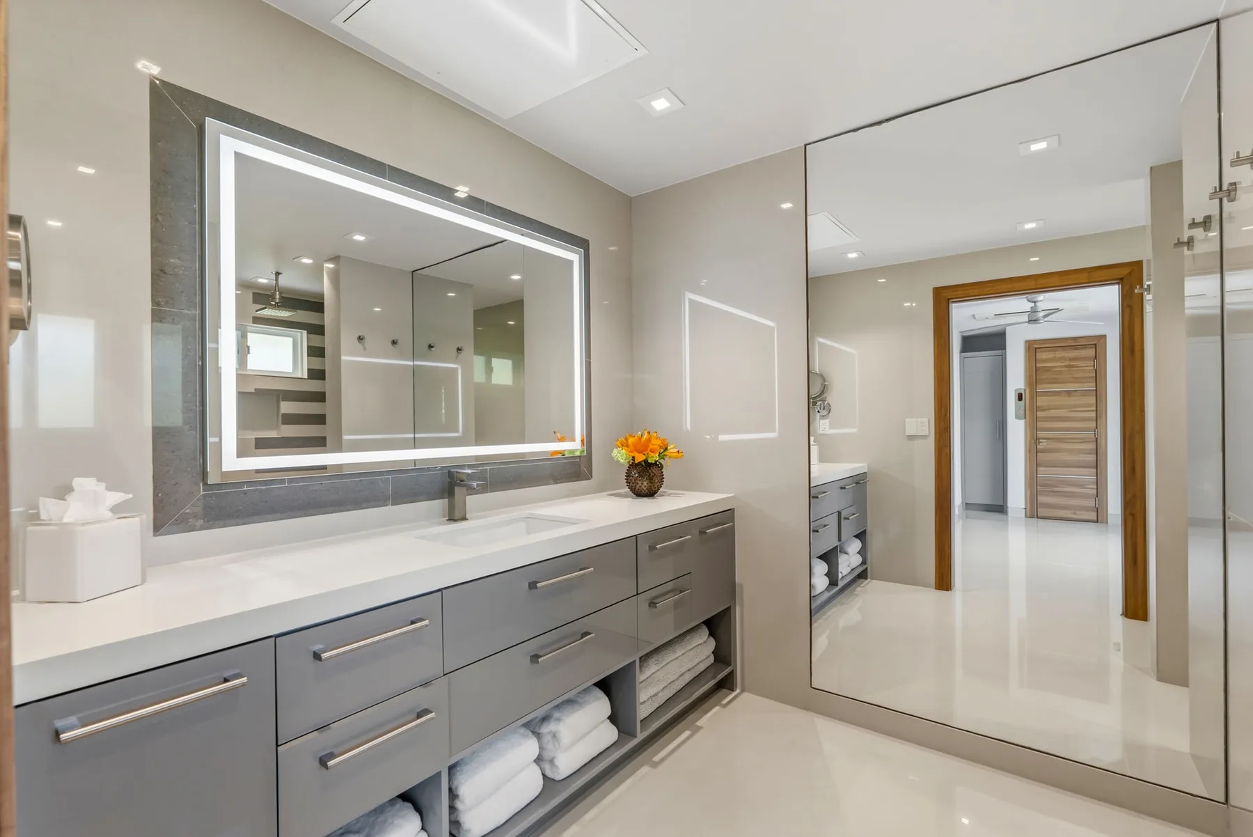 A modern bathroom vanity with a large mirror and a doorway to the adjoining room.