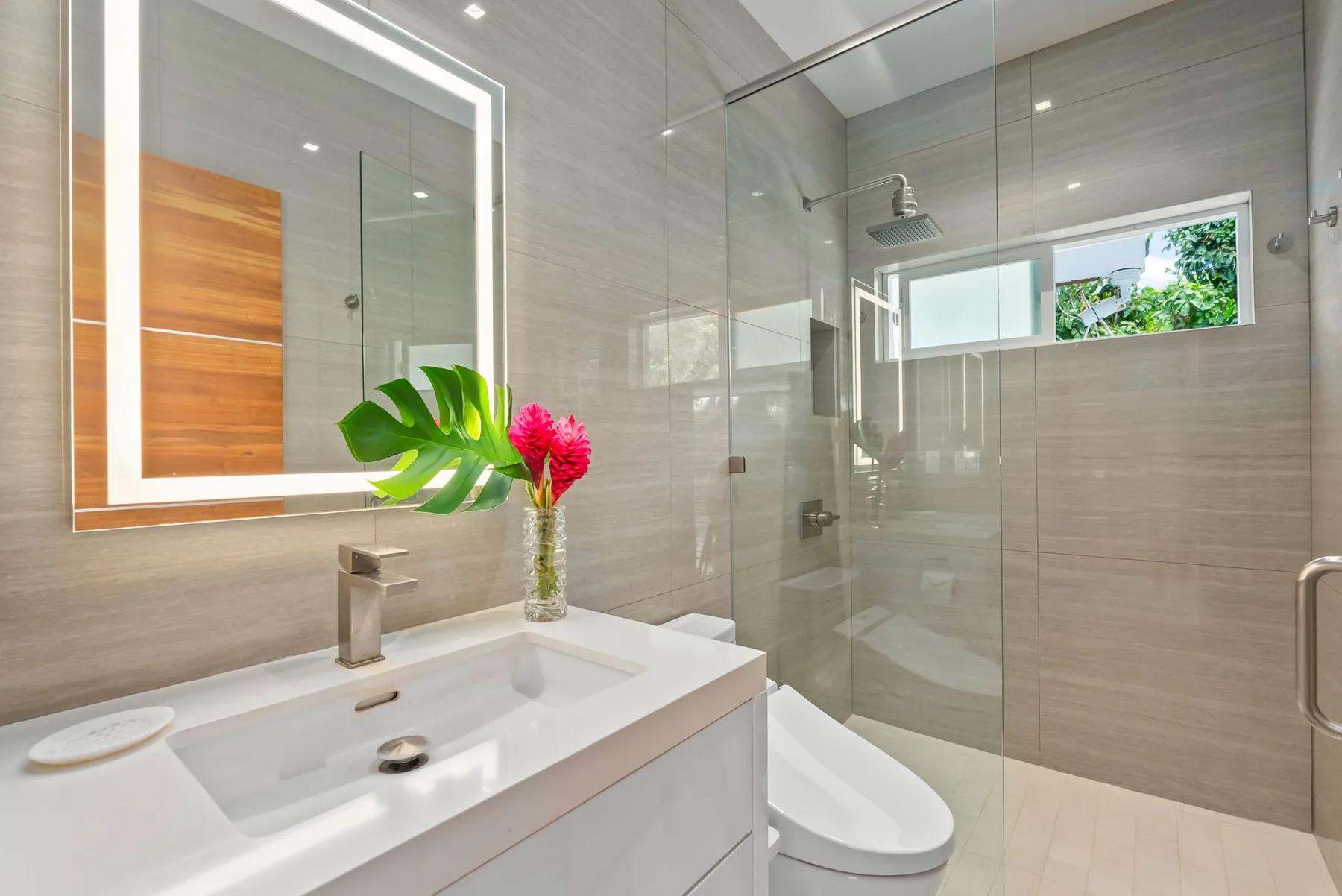 A modern bathroom with a glass shower, sink, and flower arrangement.
