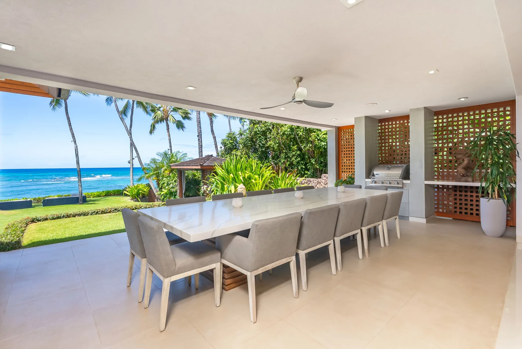 An open-air dining area with a long table overlooking the ocean and garden.