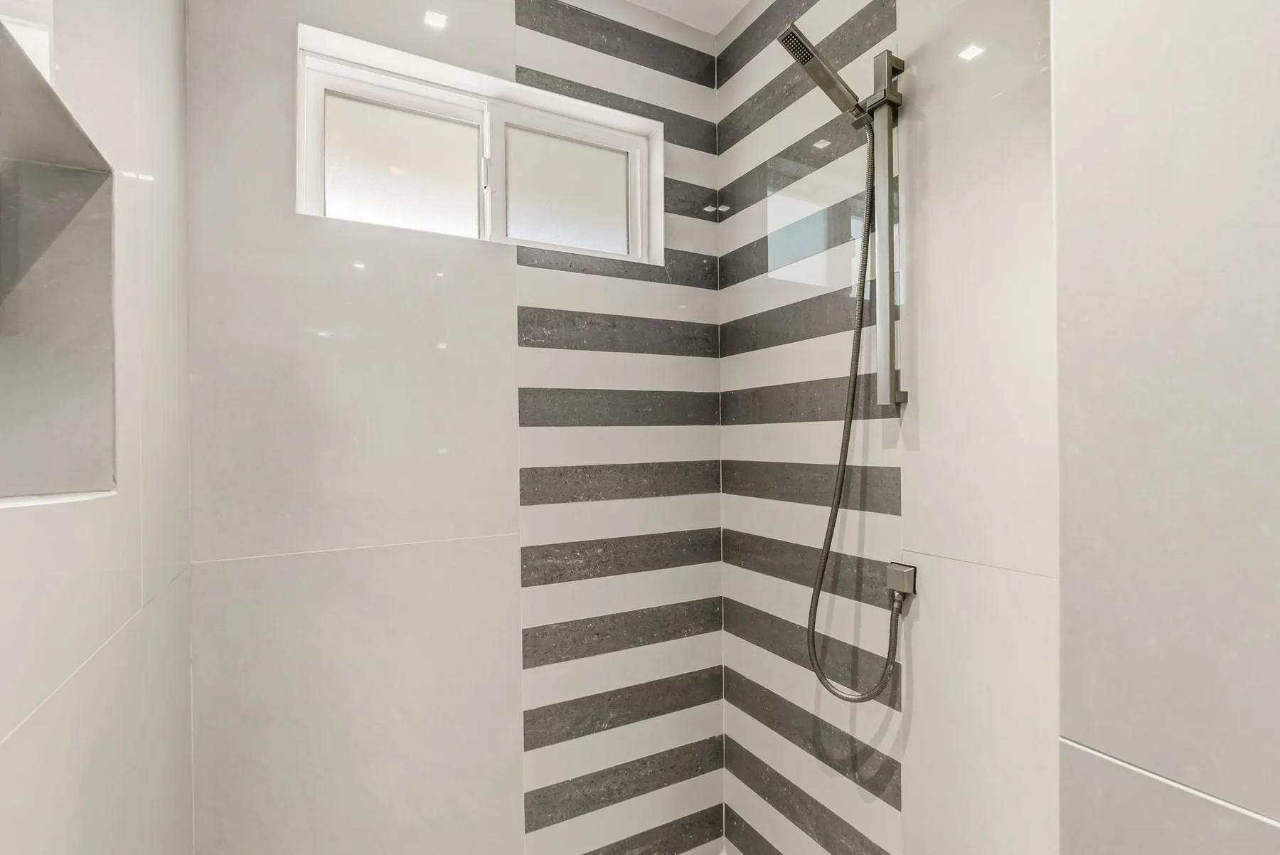 A tiled shower area features a striped wall and a small high window.