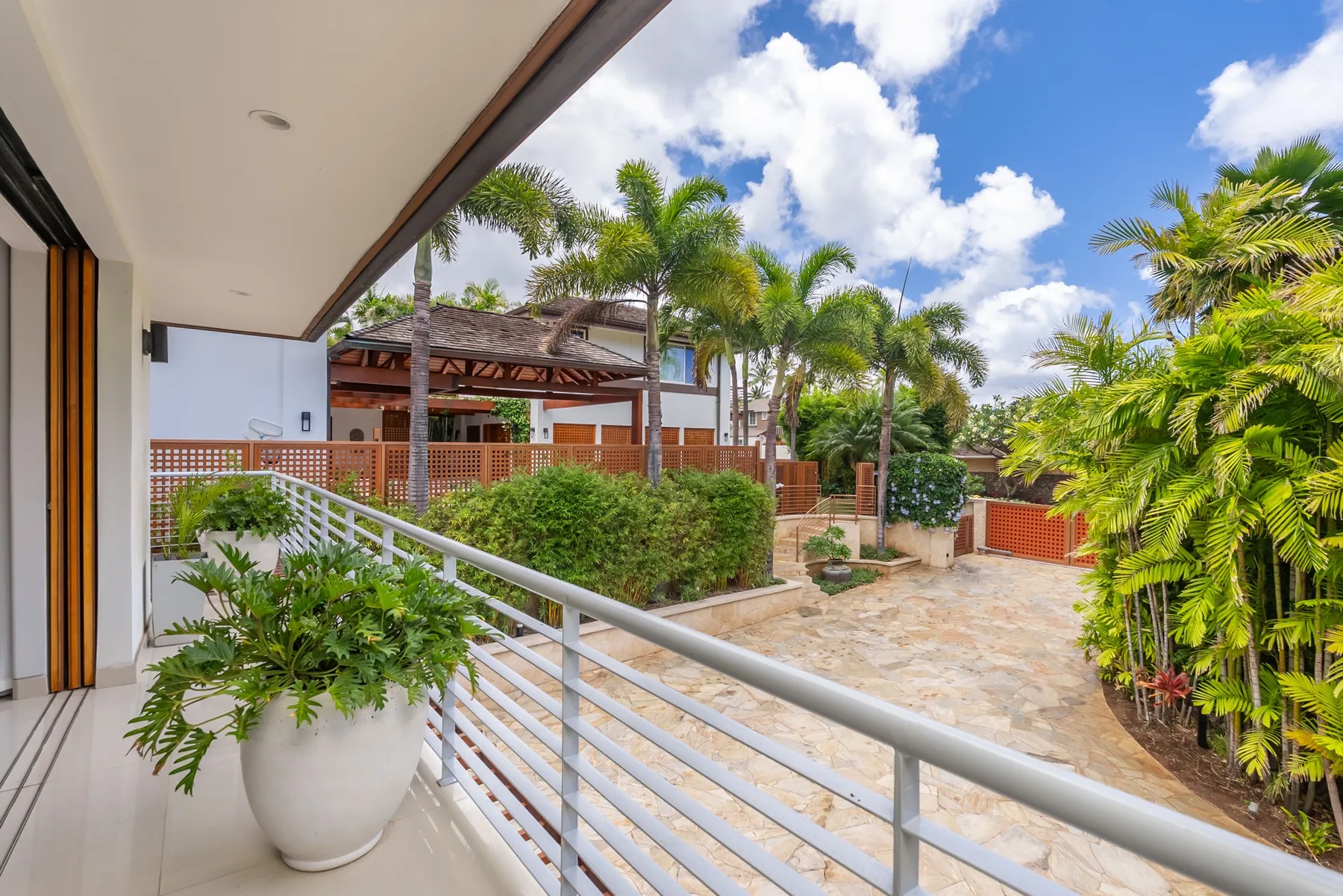 An outdoor patio overlooks a paved courtyard surrounded by palm trees and greenery.
