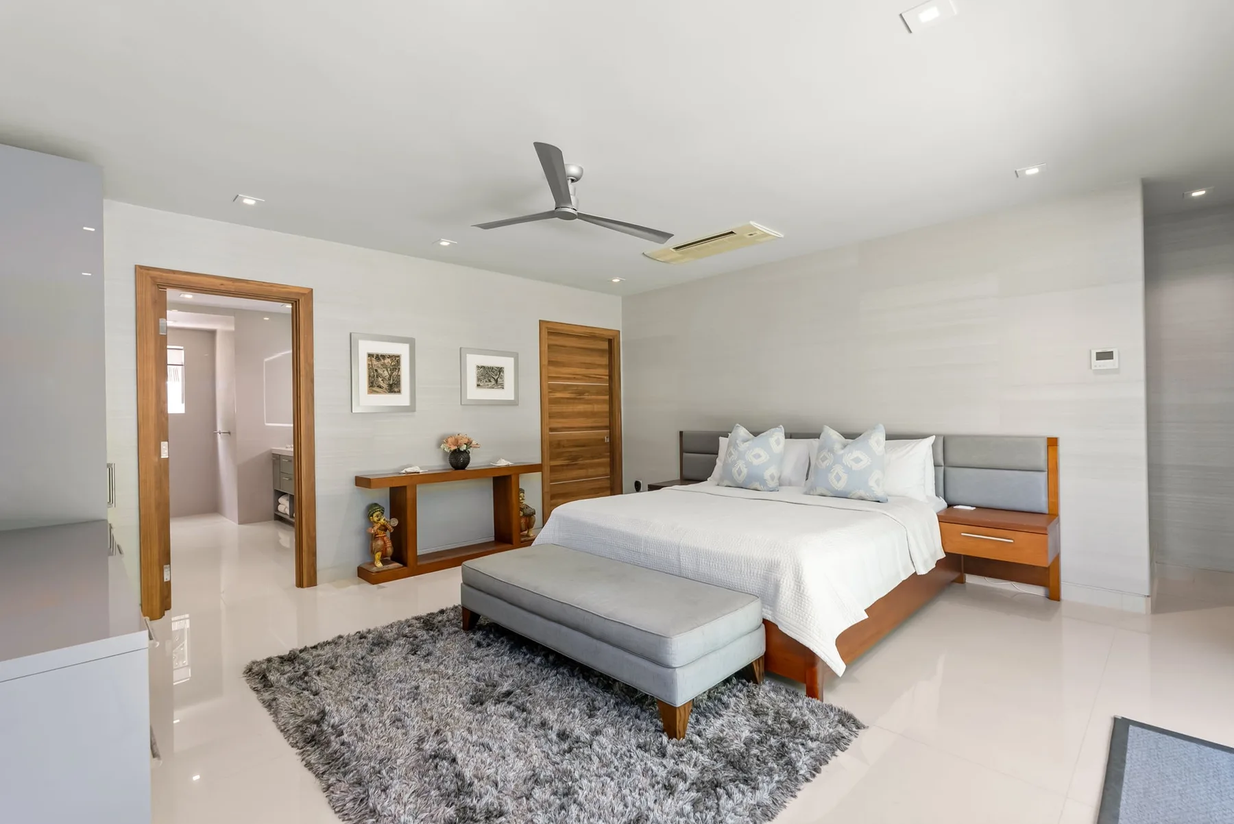A bright bedroom with a large bed, a gray rug, and a ceiling fan.