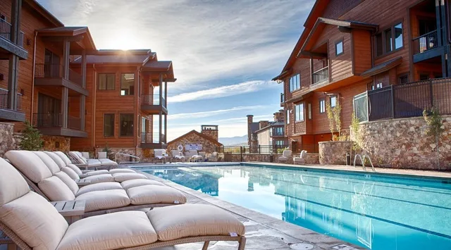 An outdoor swimming pool with cushioned loungers sits between multi-story buildings.