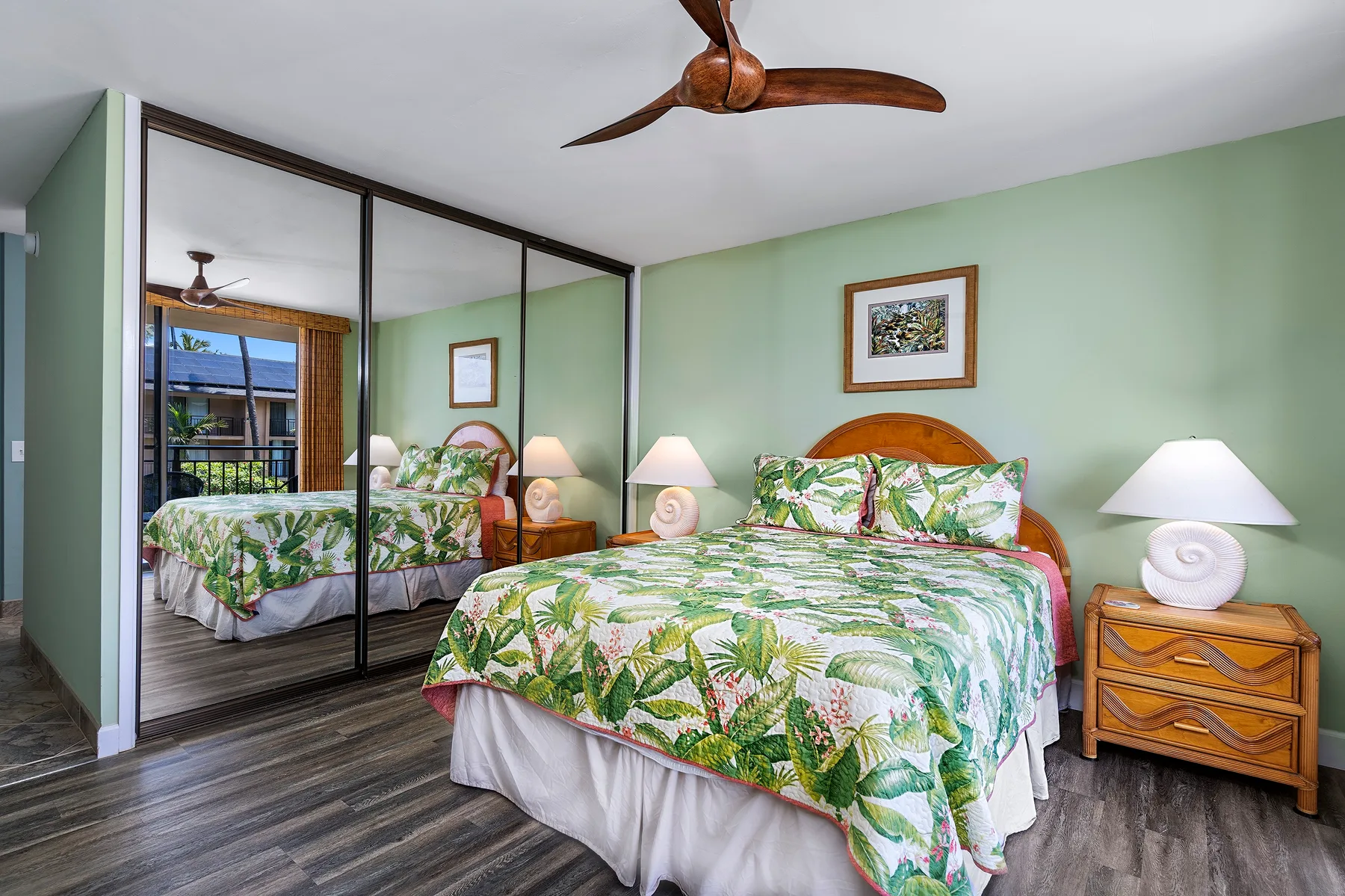 Un dormitorio con una cama vestida con ropa de cama verde estampada y puertas de armario con espejo.