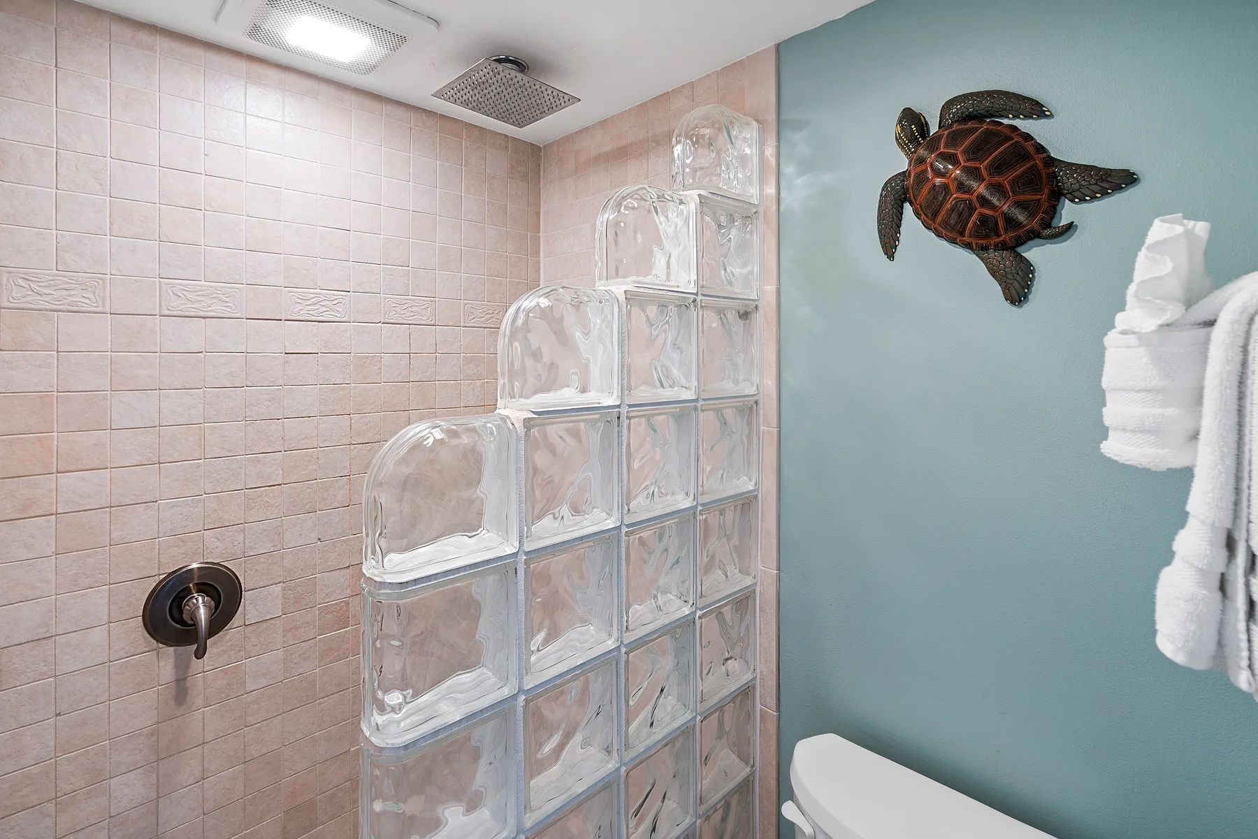 Un baño con azulejos, una división de bloques de vidrio y una toalla colgada en la pared.