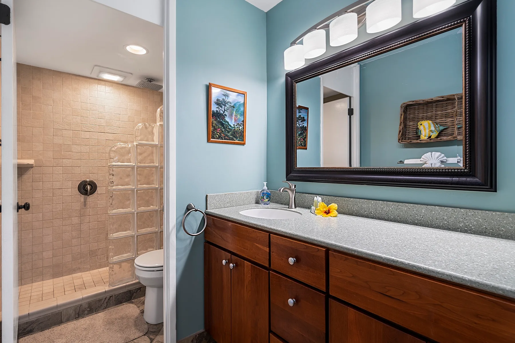 Un tocador de baño con un espejo grande está junto a una ducha revestida de azulejos.