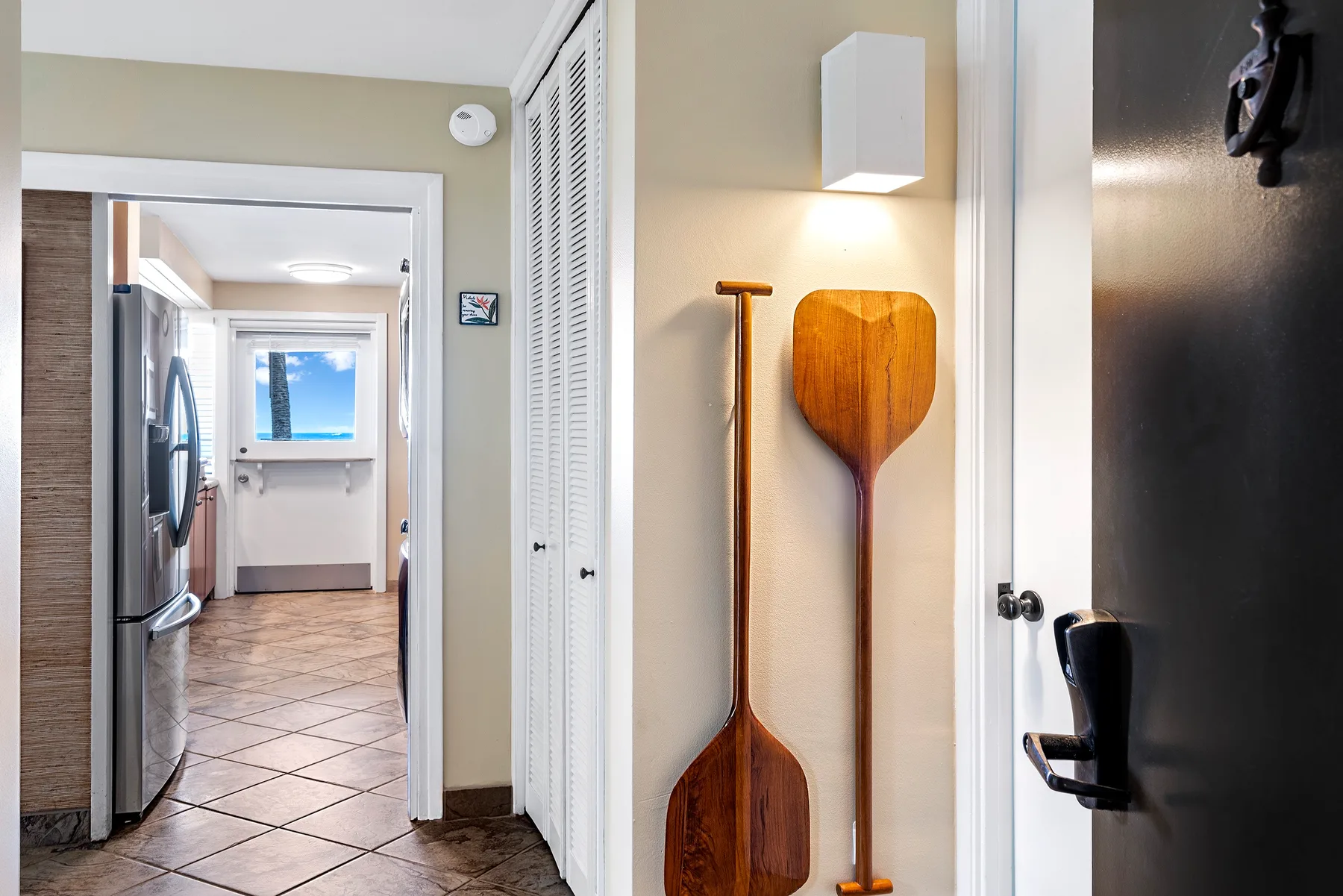 Un pasillo luminoso da a una cocina, con dos remos de madera en la pared.