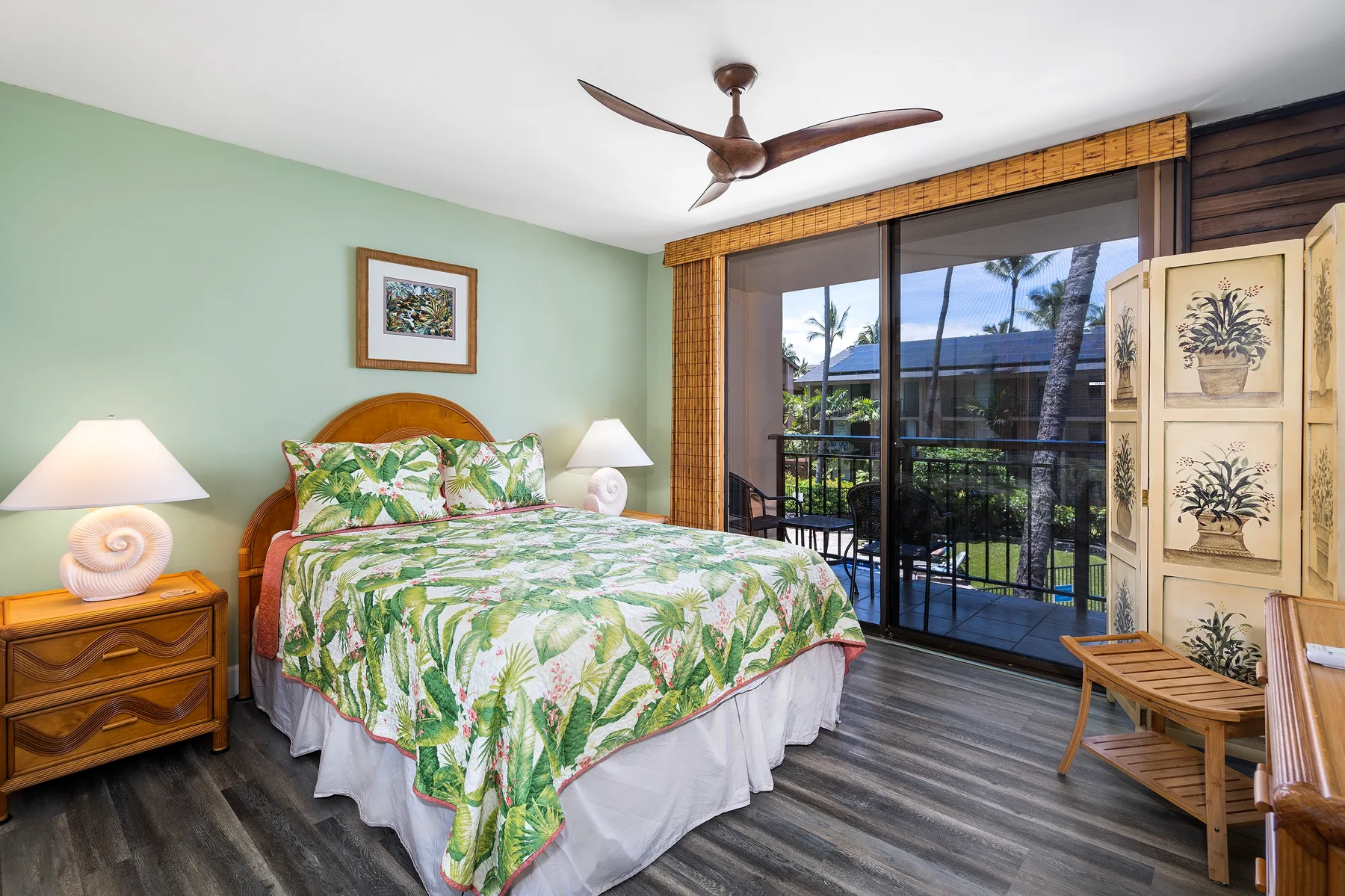 Un dormitorio con una cama estampada de motivos tropicales junto a puertas corredizas de vidrio.