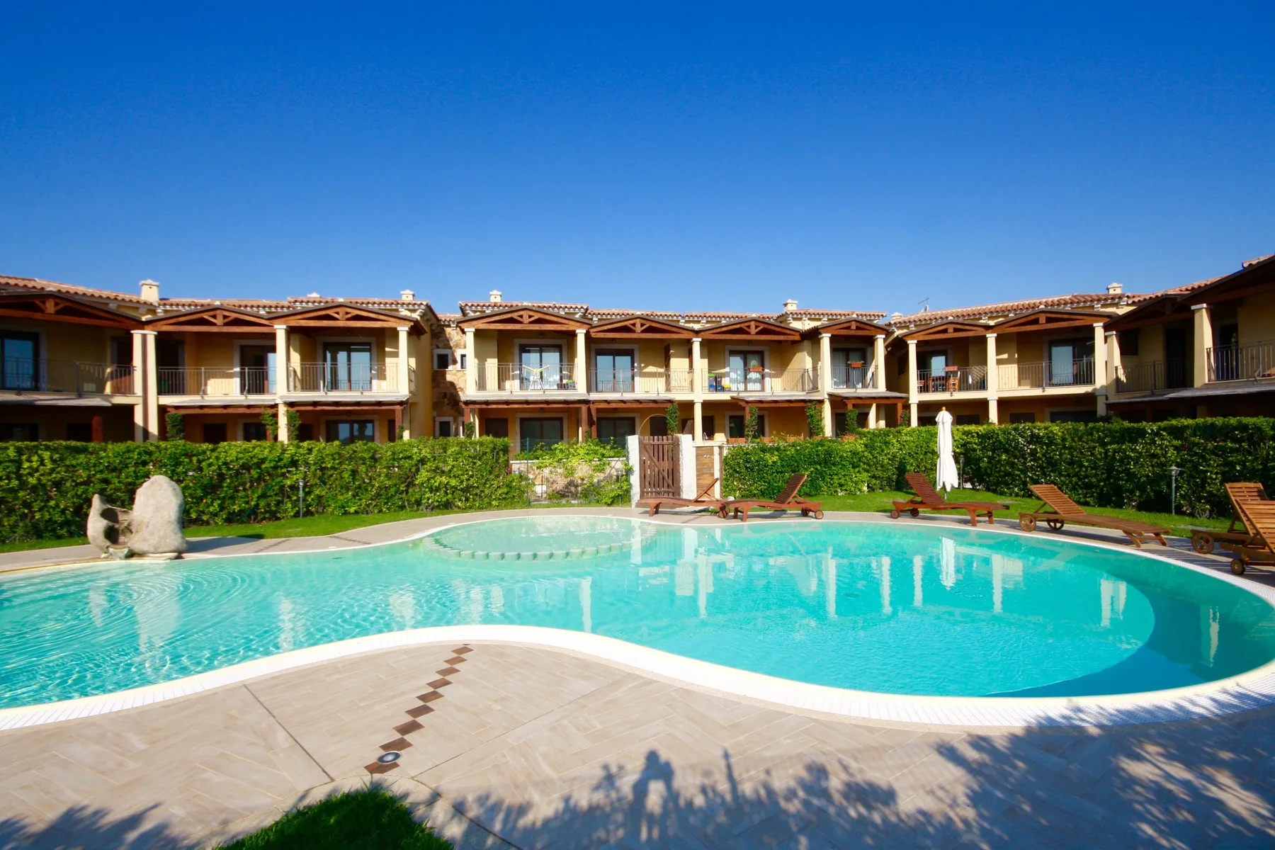 Una piscina exterior curva se encuentra frente a una fila de edificios de apartamentos.