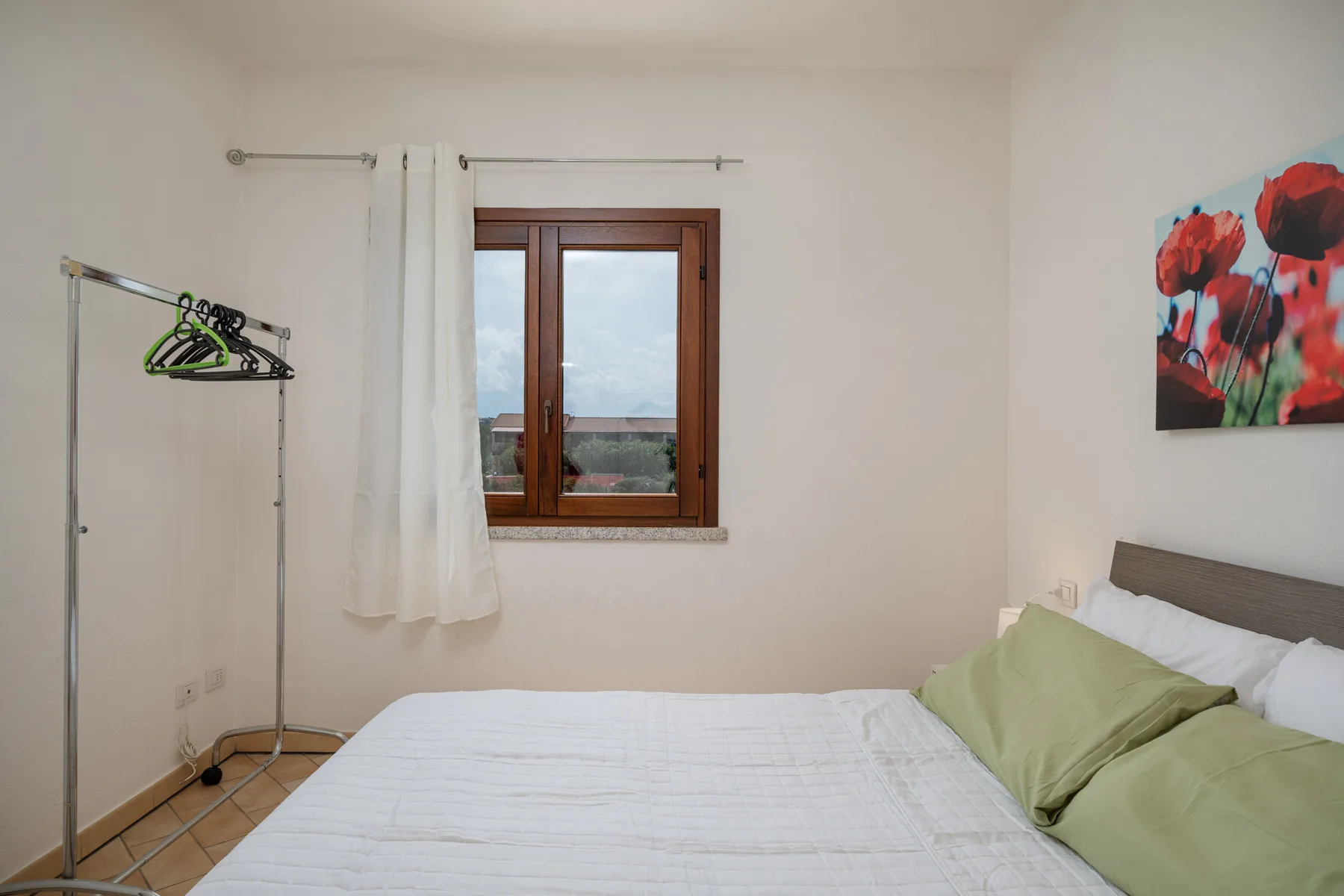 Un dormitorio con una cama, almohadas verdes y una ventana con cortinas.