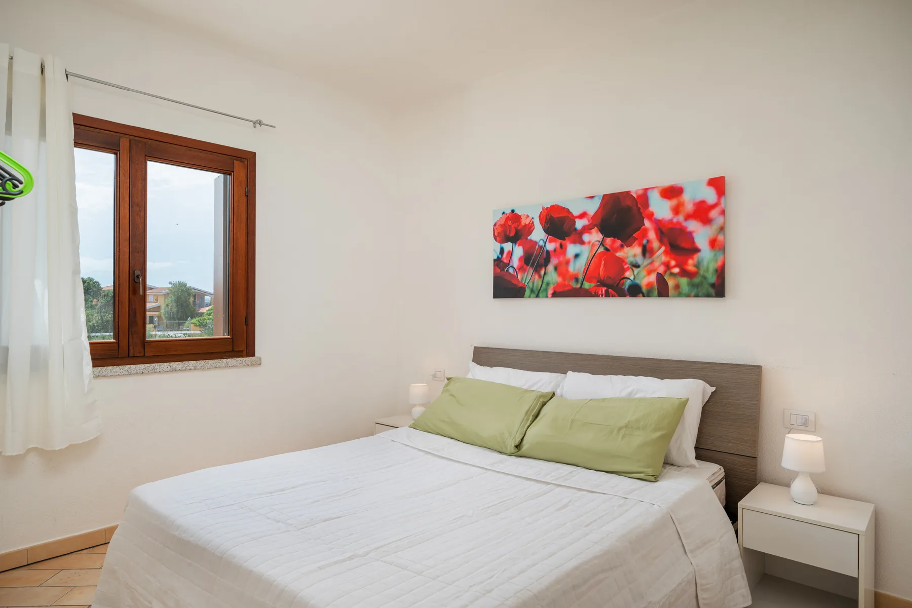 Un dormitorio con una cama, almohadas verdes y un cuadro floral colorido.