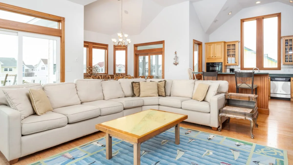 Una sala luminosa con asientos en forma de L, una mesa de centro y ventanas grandes.