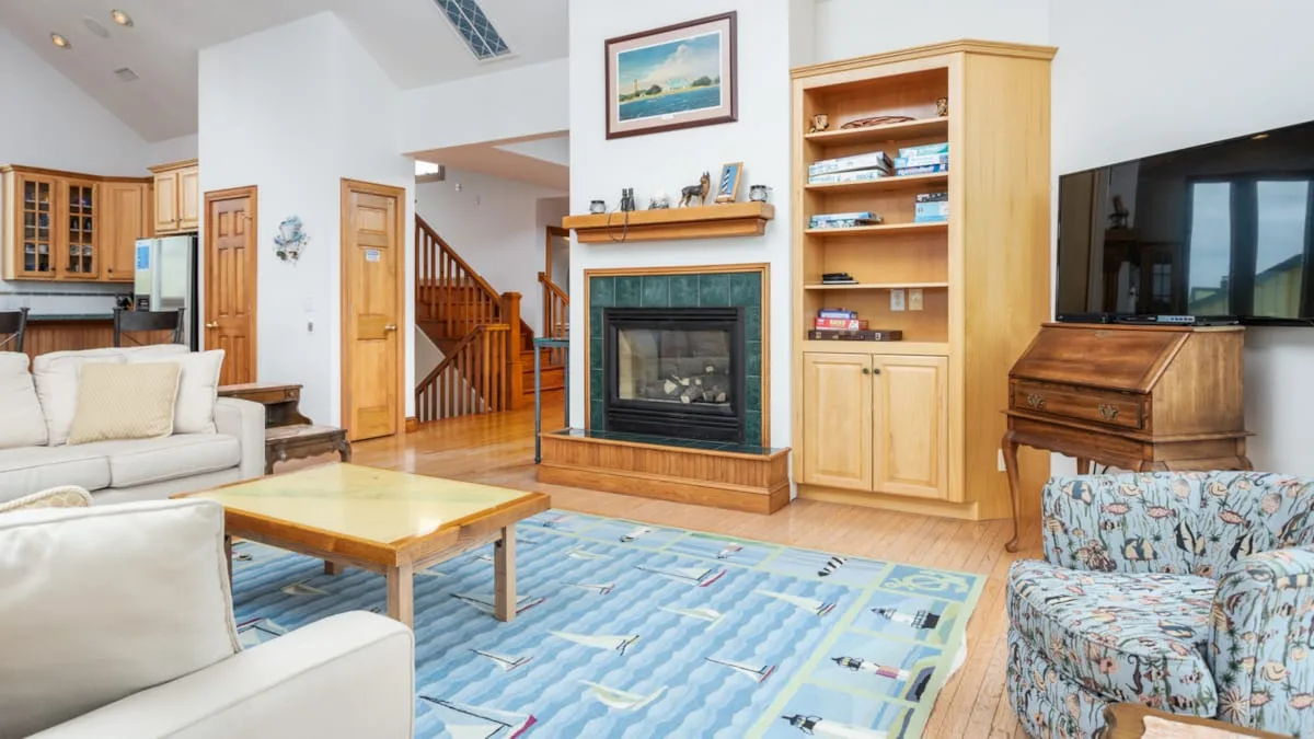 Una sala de estar con chimenea, asientos claros y una alfombra azul estampada.