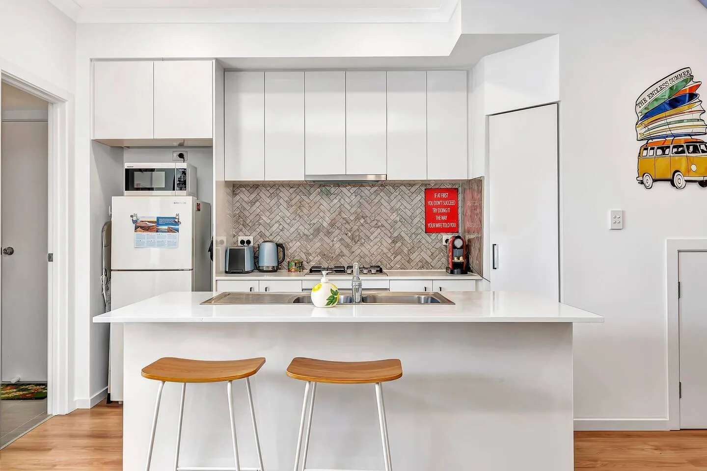 A bright white kitchen has a wide counter with two stools and cabinets.