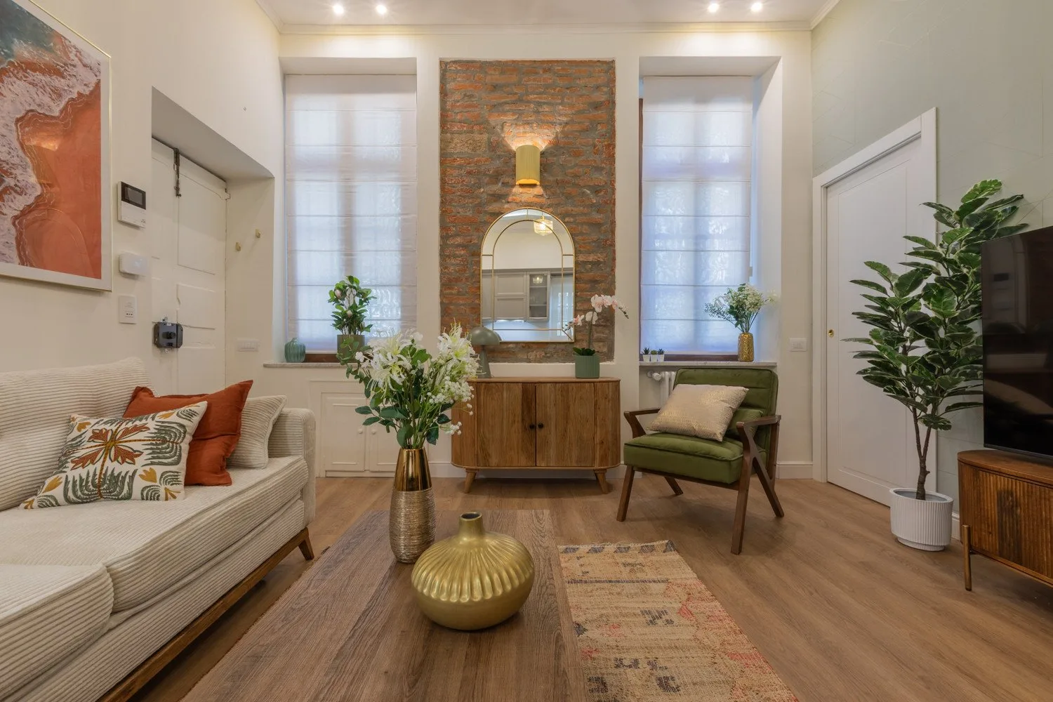 Una sala de estar luminosa con asientos, un mueble de madera y ventanas altas.