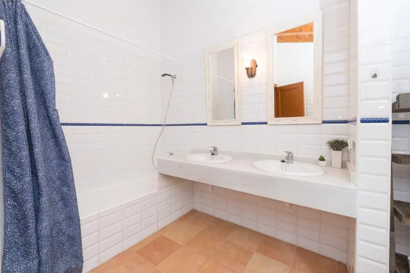 Un baño alicatado con una encimera larga, dos lavabos y una ducha.