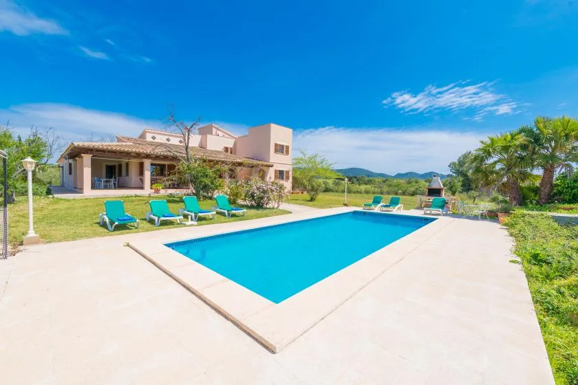 Una piscina al aire libre junto a una casa, con tumbonas en el patio.