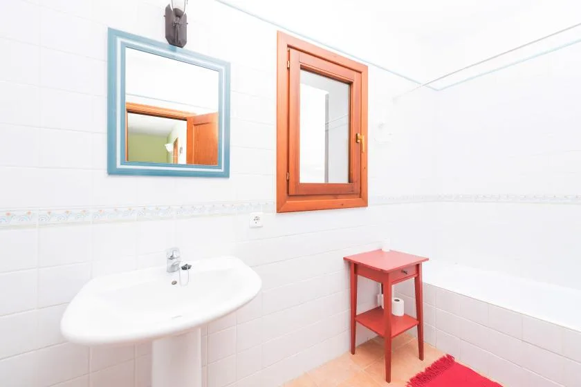 Un baño alicatado con lavabo, espejo de pared y ventana con marco de madera.