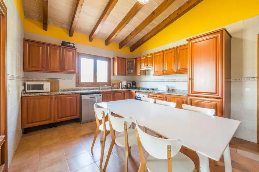 Una cocina luminosa con gabinetes de madera, una mesa grande y vigas expuestas en el techo.
