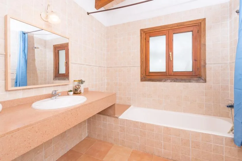 Un baño alicatado con bañera, lavabo y ventana con marco de madera.
