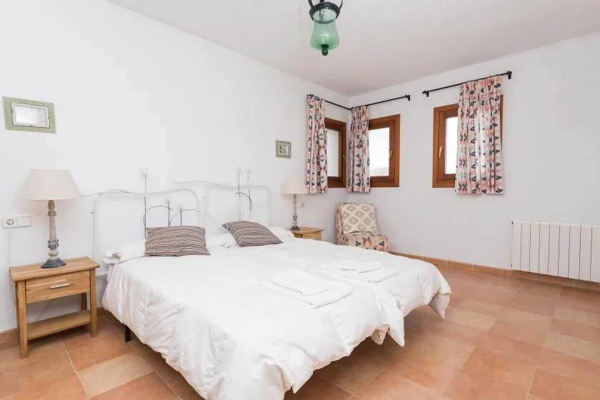 Un dormitorio luminoso con una cama doble, mesitas de noche y ventanas con cortinas estampadas.