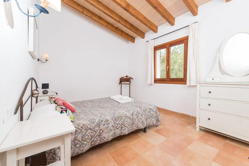 Un dormitorio con una cama bajo vigas de madera vistas y una ventana.