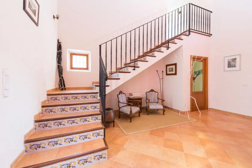 Un interior luminoso con una escalera de azulejos, barandilla metálica y asientos debajo.
